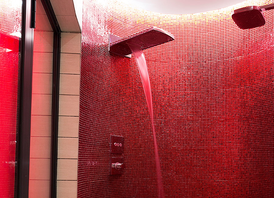 Curved shower niche clad in small red glass mosaic tiles with rainfall fixture 