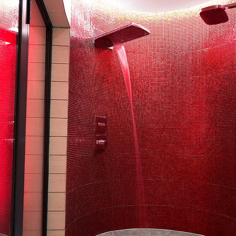 Modern shower head pouring water against vibrant red mosaic tile wall