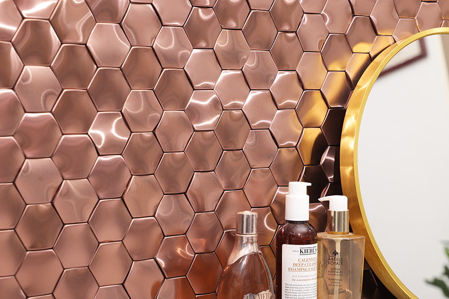 Rose‑gold metal hexagon backsplash accented by skincare bottles and part of a round mirror