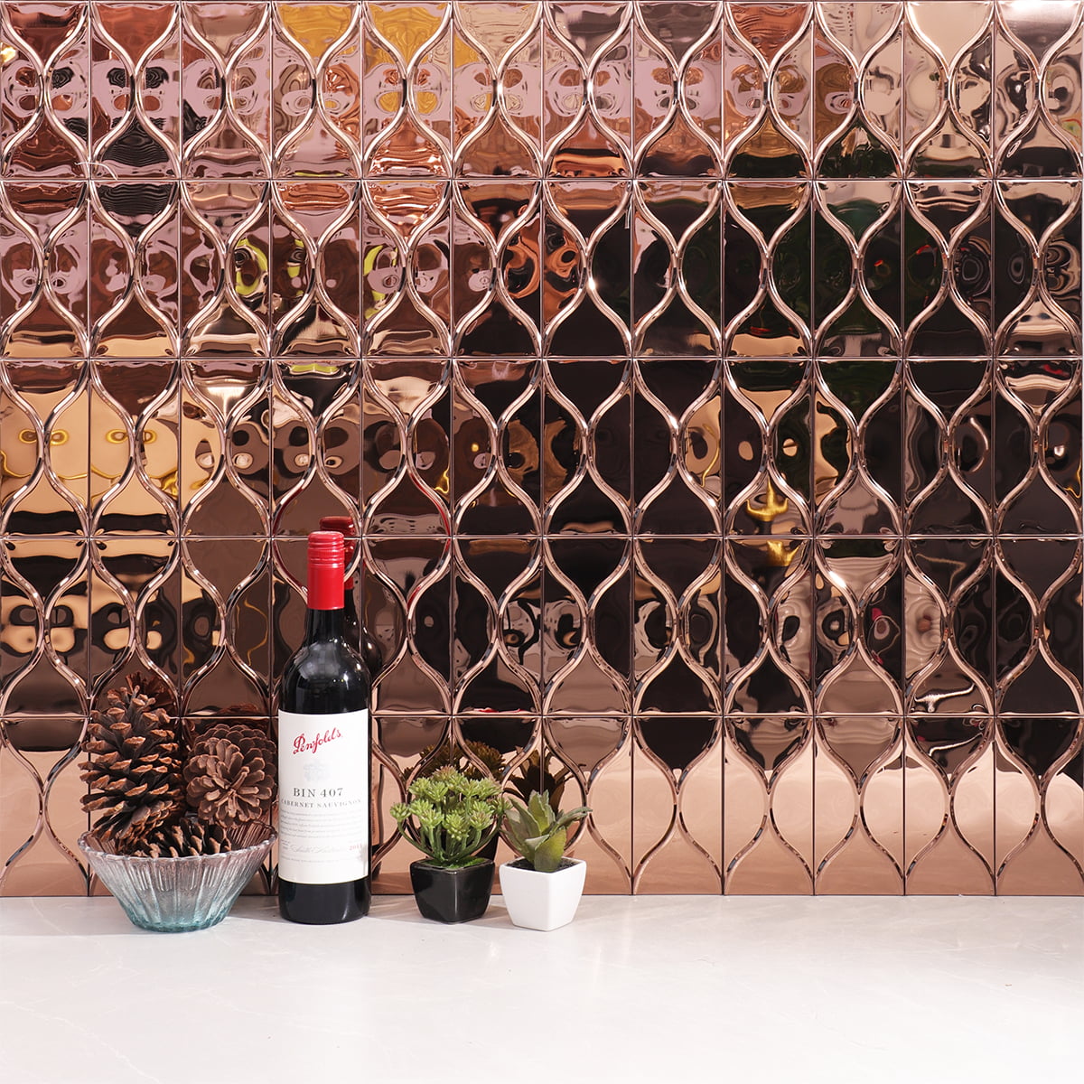 Rose gold metallic tiles arranged in a grid pattern, with decorative plants in the foreground