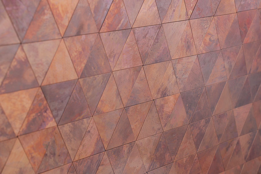 Rusted copper triangle metal tiles with warm oxidized tones on a feature wall