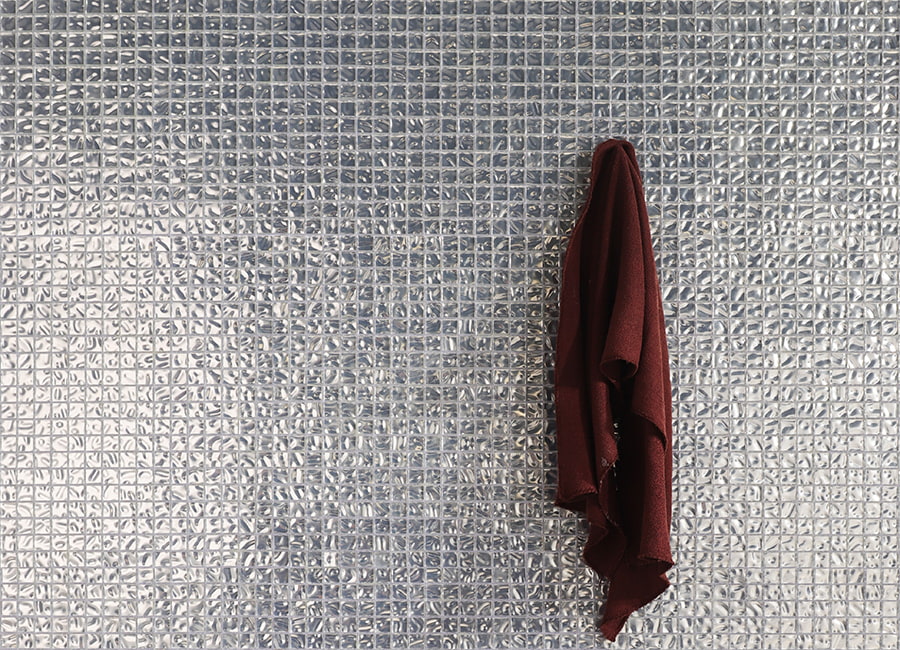 Glossy silver foil glass mosaic tiles backdrop featuring a hanging burgundy towel.