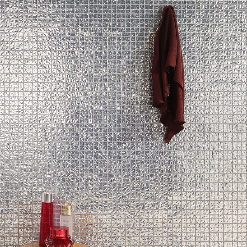 A glossy silver foil glass mosaic tile wall accented by red cosmetic bottles at the base.