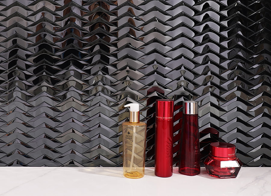 Sleek stainless steel chevron pattern wall featuring skincare and makeup bottles on a white surface.