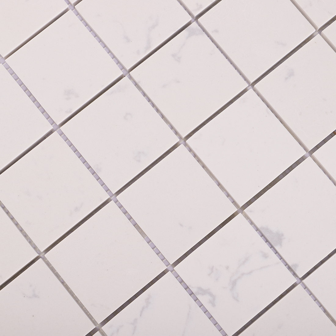 Diagonal close-up showing subtle veining of white engineered marble tiles.