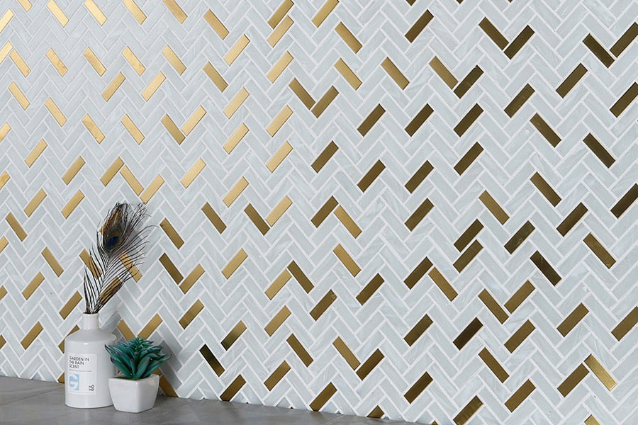 White marble and gold metal herringbone mosaic tile backsplash behind countertop decor 