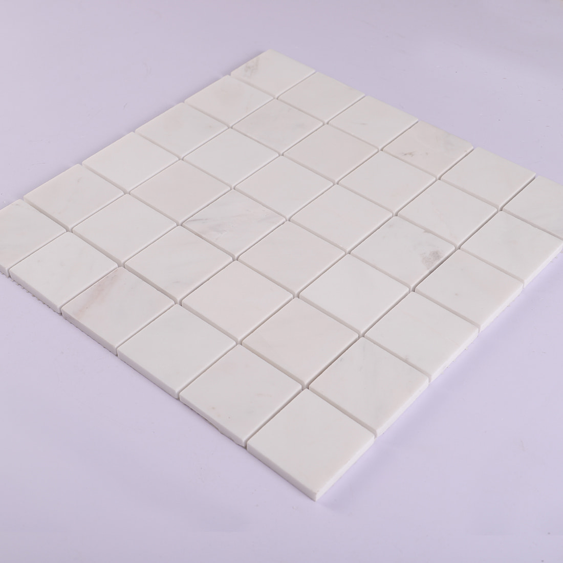Angled view of white marble square mosaic tile sheet.