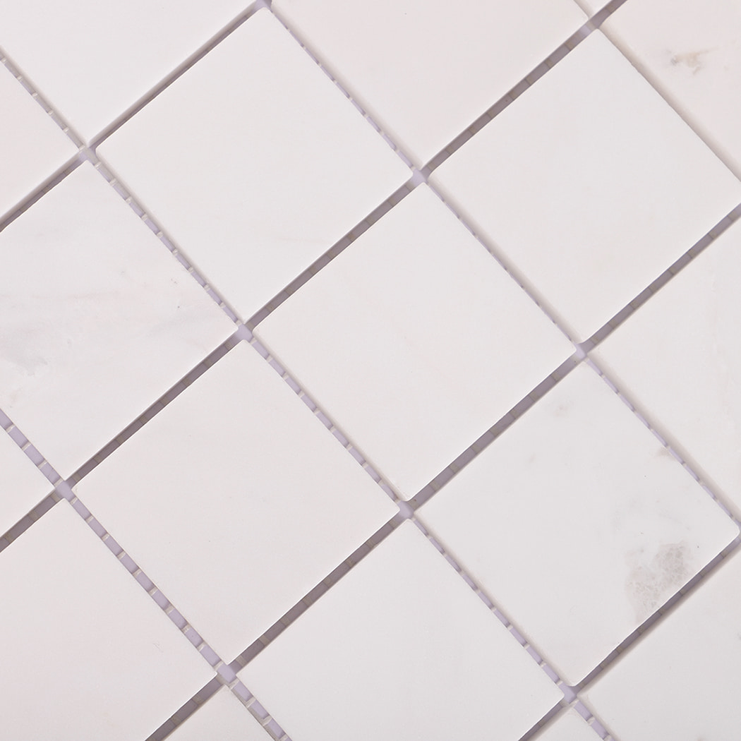 Diagonal close-up of white marble square mosaic tiles.