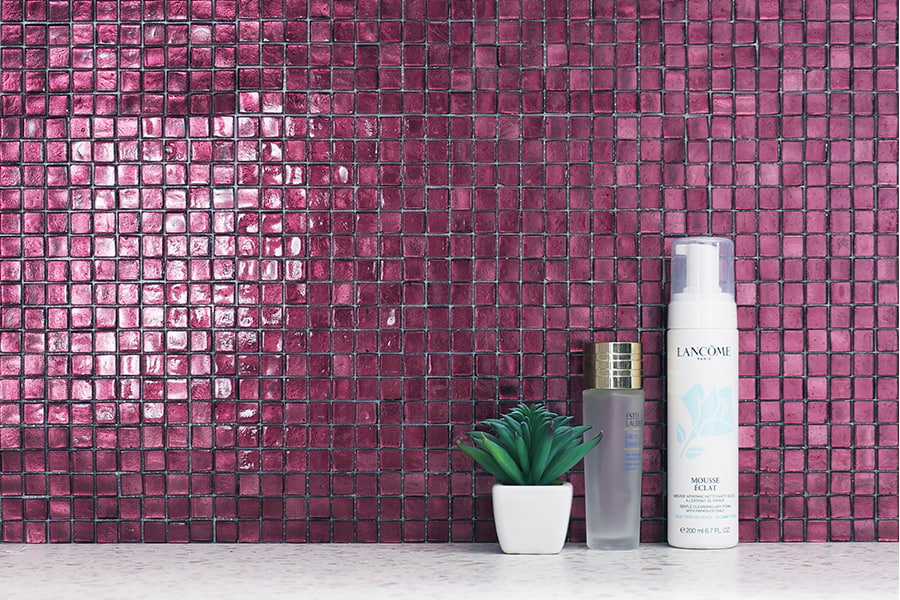 Wide purple glass mosaic backsplash behind skincare bottles and a potted succulent