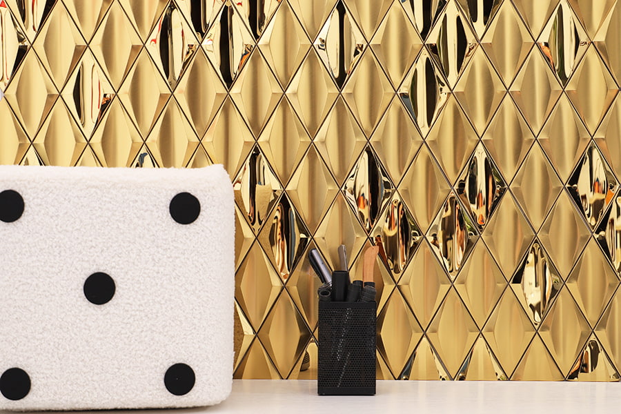 Wide view of gold diamond metal tile wall behind white cushion and black pen holder on desk