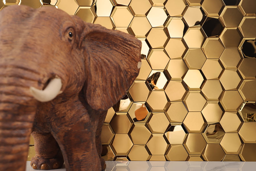 Side view of a wooden elephant figure standing against a backdrop of shiny gold hexagon metal tiles