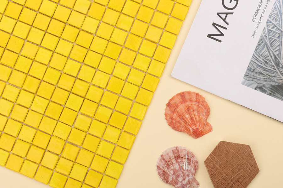 Close-up of yellow glass mosaic tiles with decorative shells and paper on side