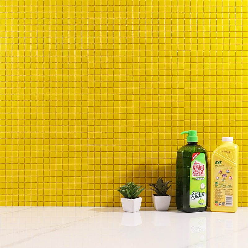 Glossy yellow square mosaic backsplash tiles behind white marble counter