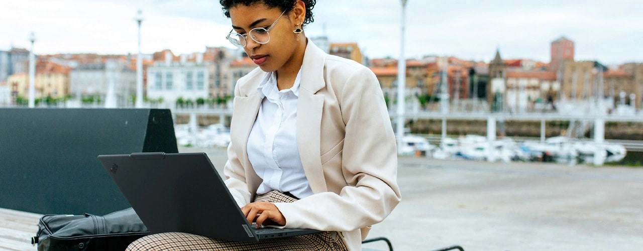 Front view of a professional working on the Lenovo ThinkPad T14s Gen5 (14&rdquo; Intel) Eclipse Black laptop placed on its lap, sitting outdoors, focusing its carbon-fiber-based top cover & slim profile.
