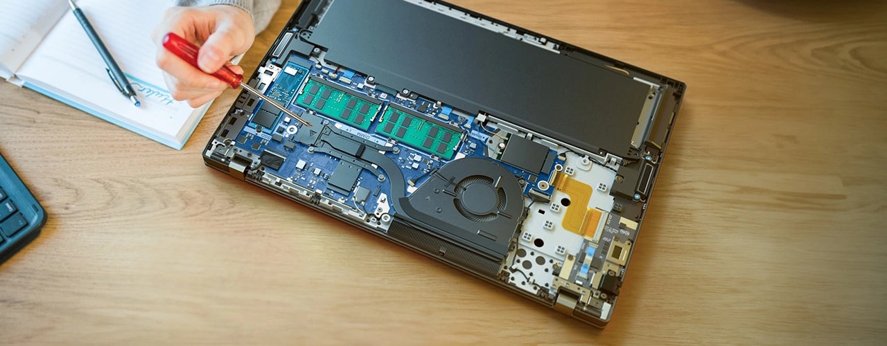 Lenovo ThinkPad T16 Gen 3 (16" Intel) laptop &mdash; on a desk, cover removed to show internal components, with a hand pointing a screwdriver