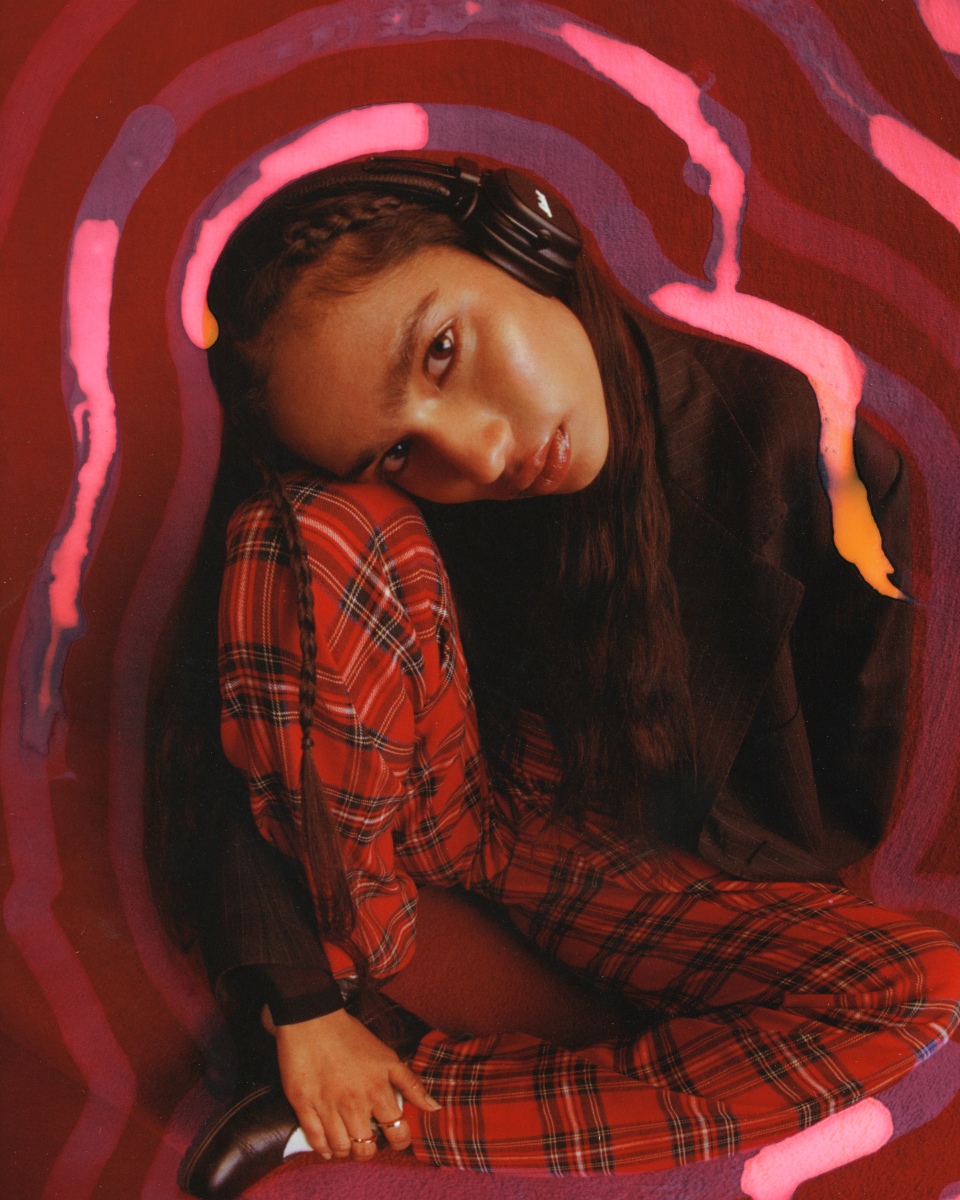 Woman in a plaid outfit sitting and wearing Marshall Major V Black on-ear headphones.