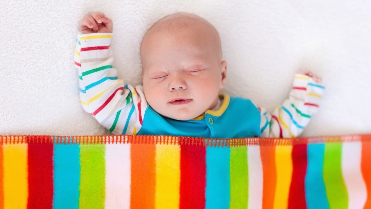 Baby sleeping peacefully under a vibrant, colourful, and striped blanket