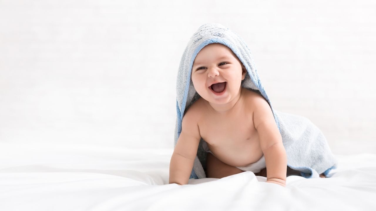 A baby smiling happily while wrapped in a cosy hooded baby towel