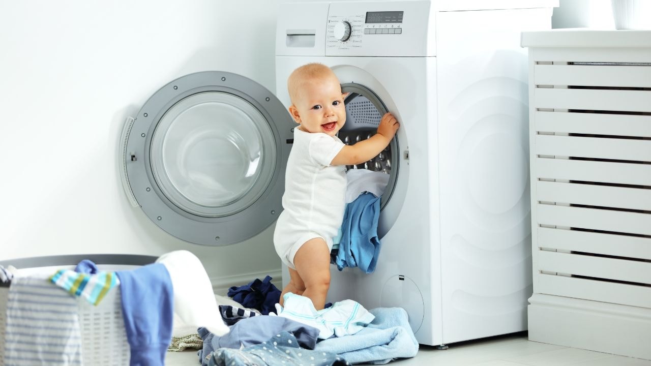 Baby playing near a washing machine, highlighting the machine-washable blankets for busy parents.