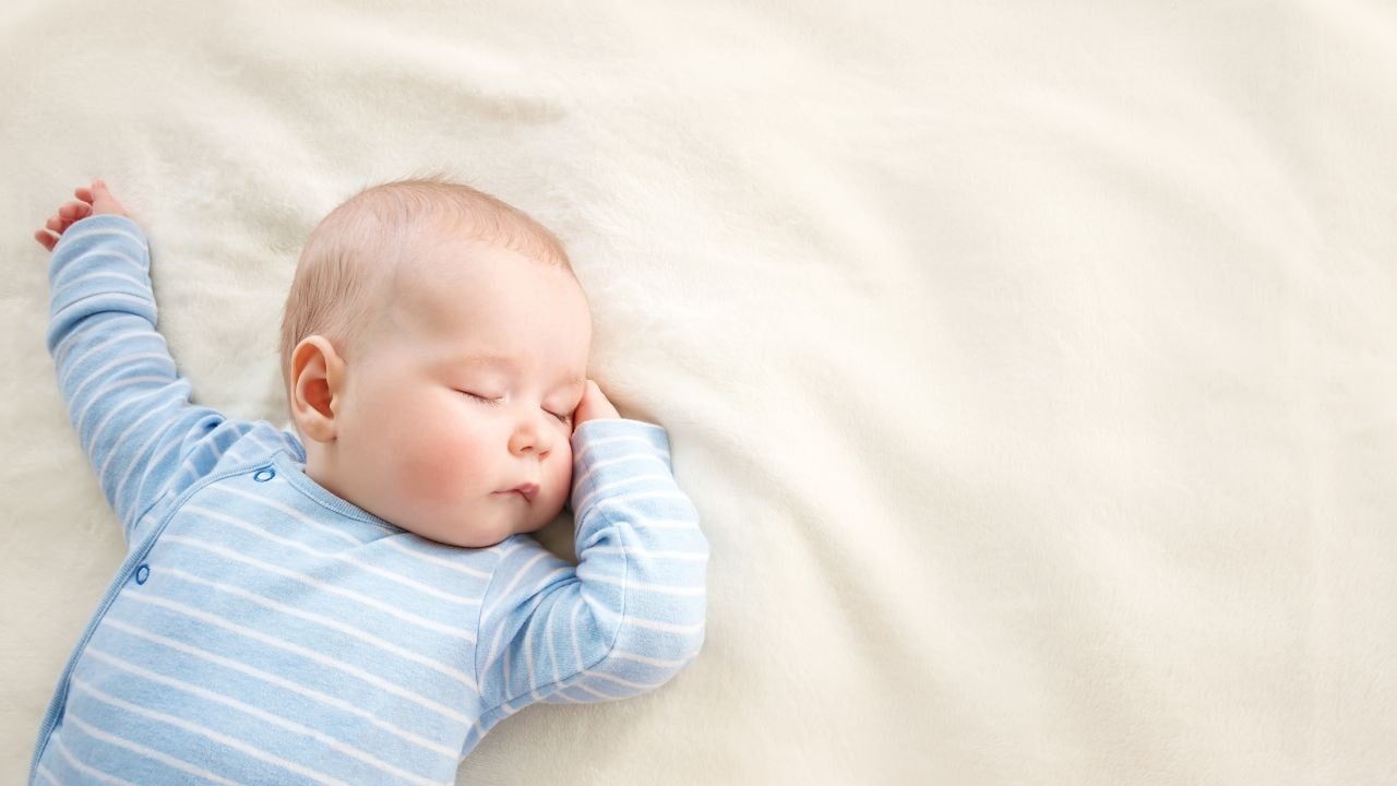Sleeping baby in a sleep sack and under a soft baby swaddle 