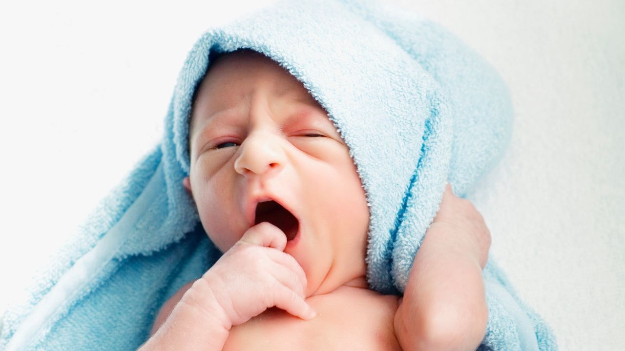 A yawning newborn, feeling comfy being wrapped in one of those soft towels with a hood