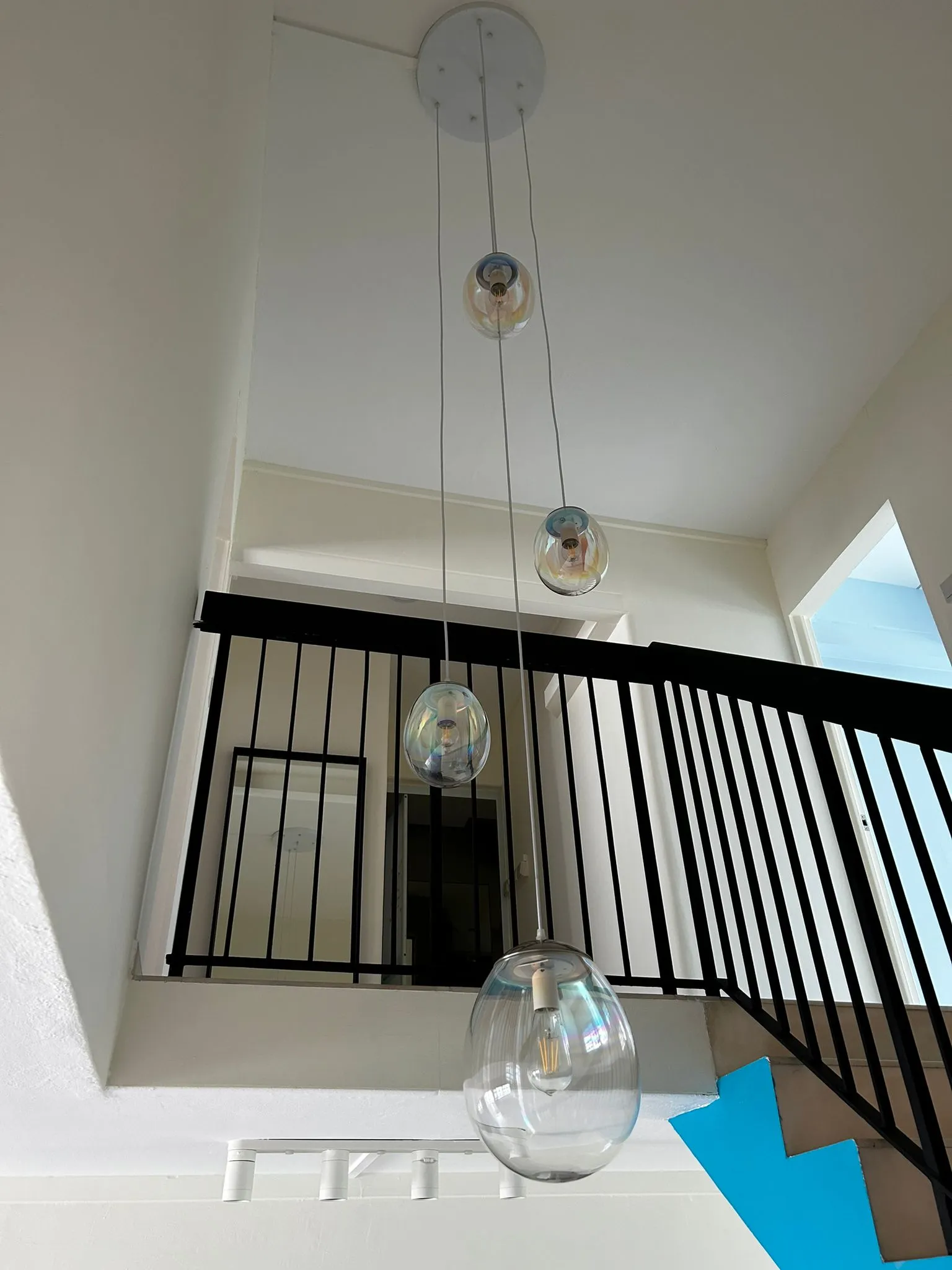 Elegant glass pendant lights hanging in a bright, modern duplex with a black railing and high ceiling.