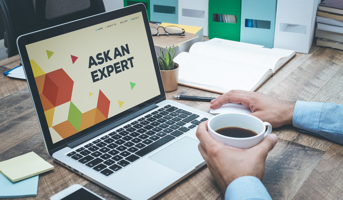 Person using laptop with “Ask an Expert” on the screen while holding a coffee mug