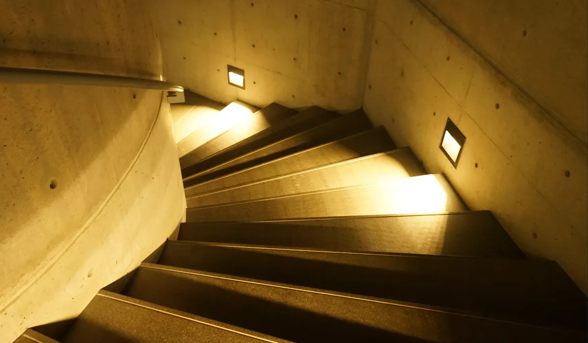 Curved staircase illuminated by warm recessed step lights along a concrete wall