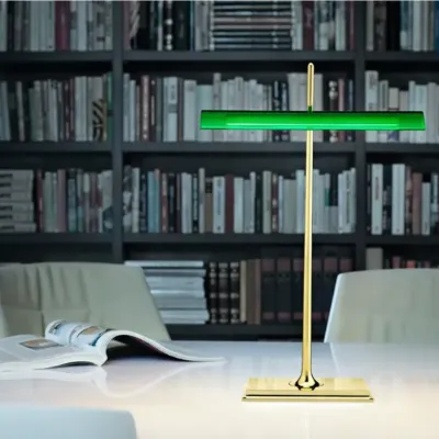 Modern banker’s lamp with green glass shade and brass base, illuminating a stylish library setting.