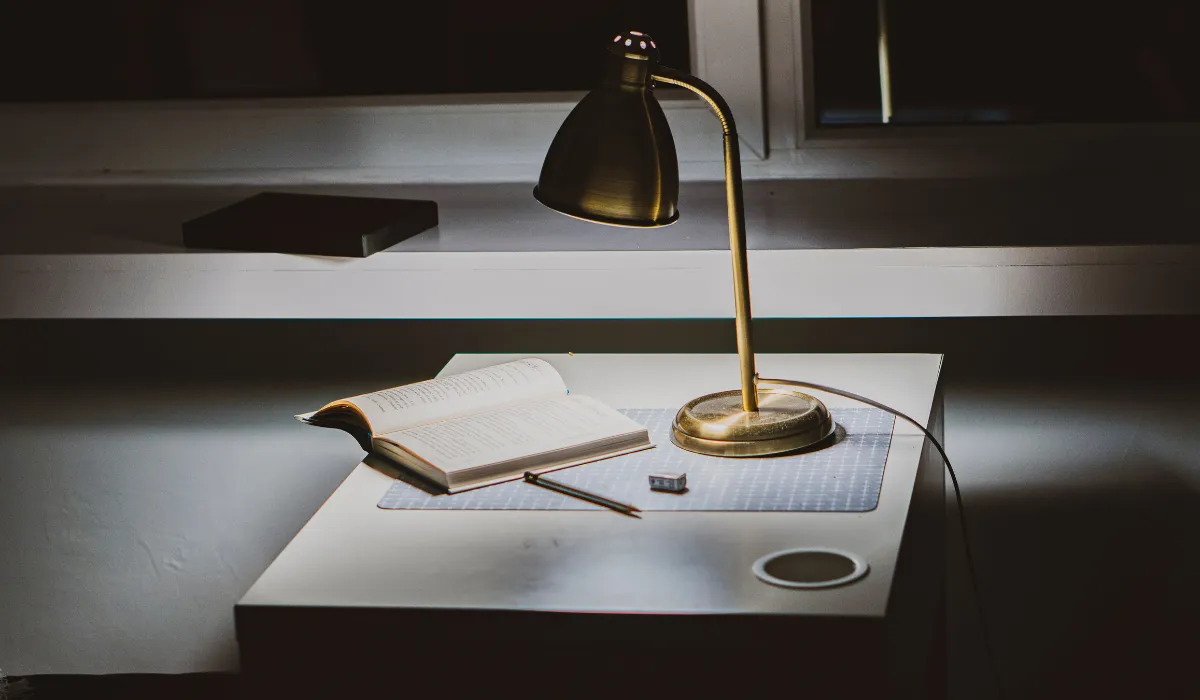 Vintage brass desk lamp casting focused task lighting on an open book and notebook in a cozy study corner.