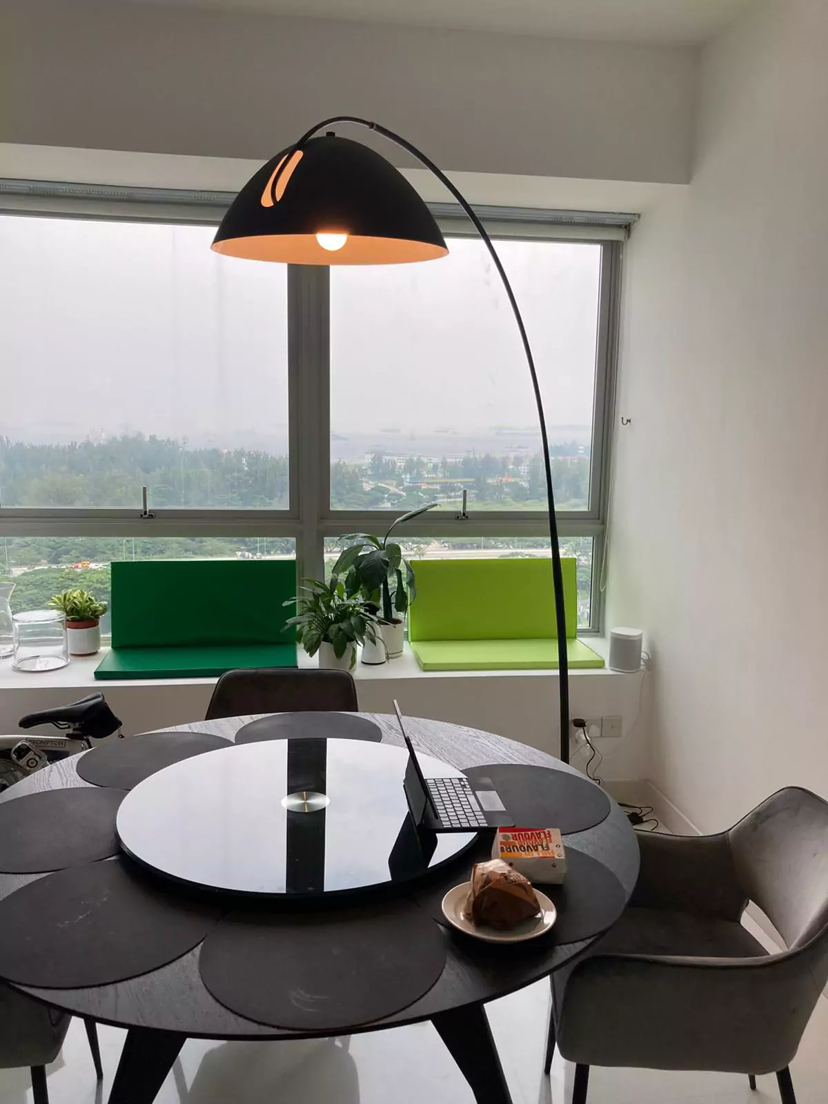 {"default":"Modern dining area featuring an arched floor lamp with a large black shade, which hovers over a circular table with a reflective surface."}