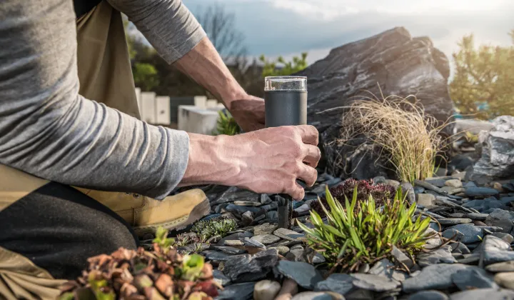Man installing a garden path light among rocks and plants