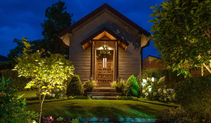 Cozy house with landscape lighting highlighting trees and entrance at night