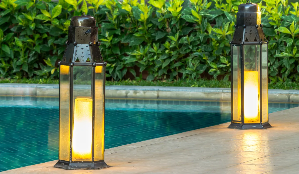 Outdoor lantern-style lights glowing beside a pool at dusk