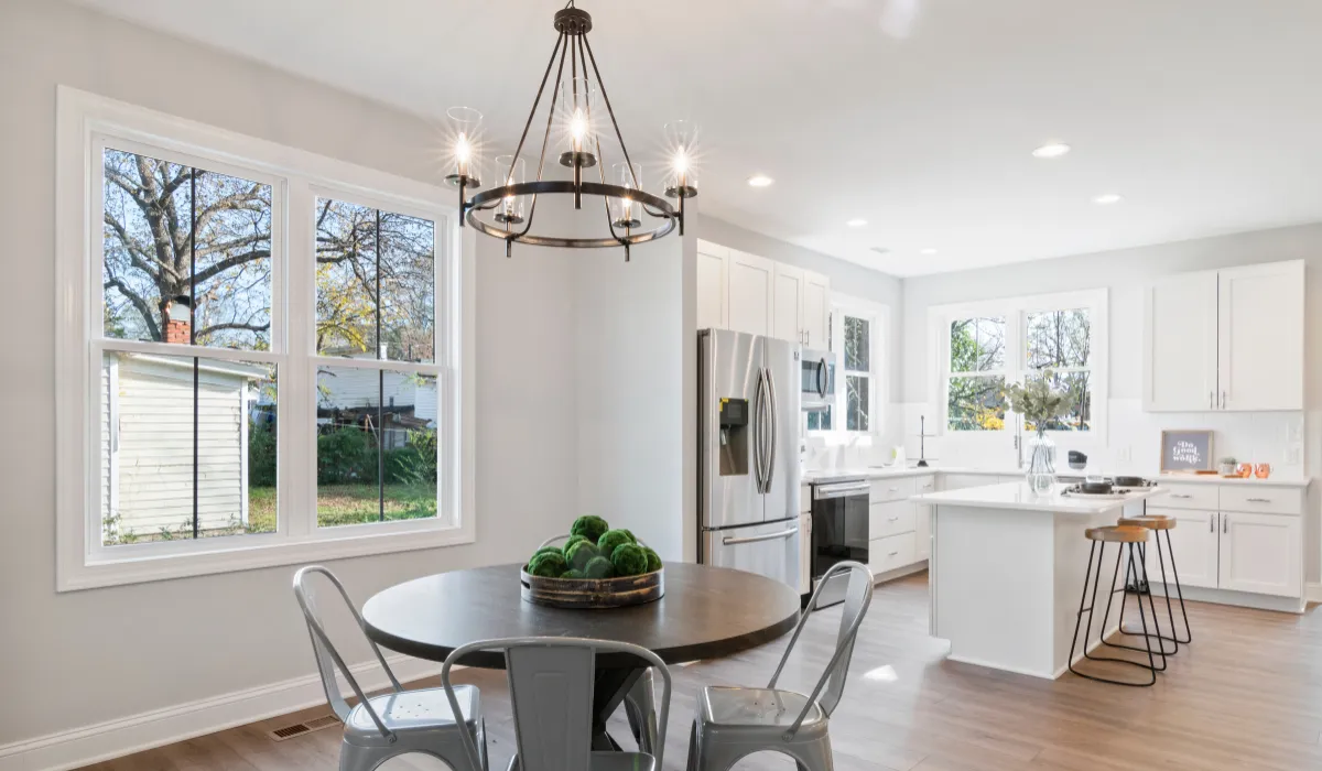 Bright kitchen-dining space with a black chandelier and metal chairs around a round table.