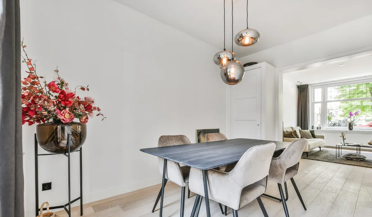 Minimalist dining room with velvet chairs and modern pendant lights in a soft neutral setting.