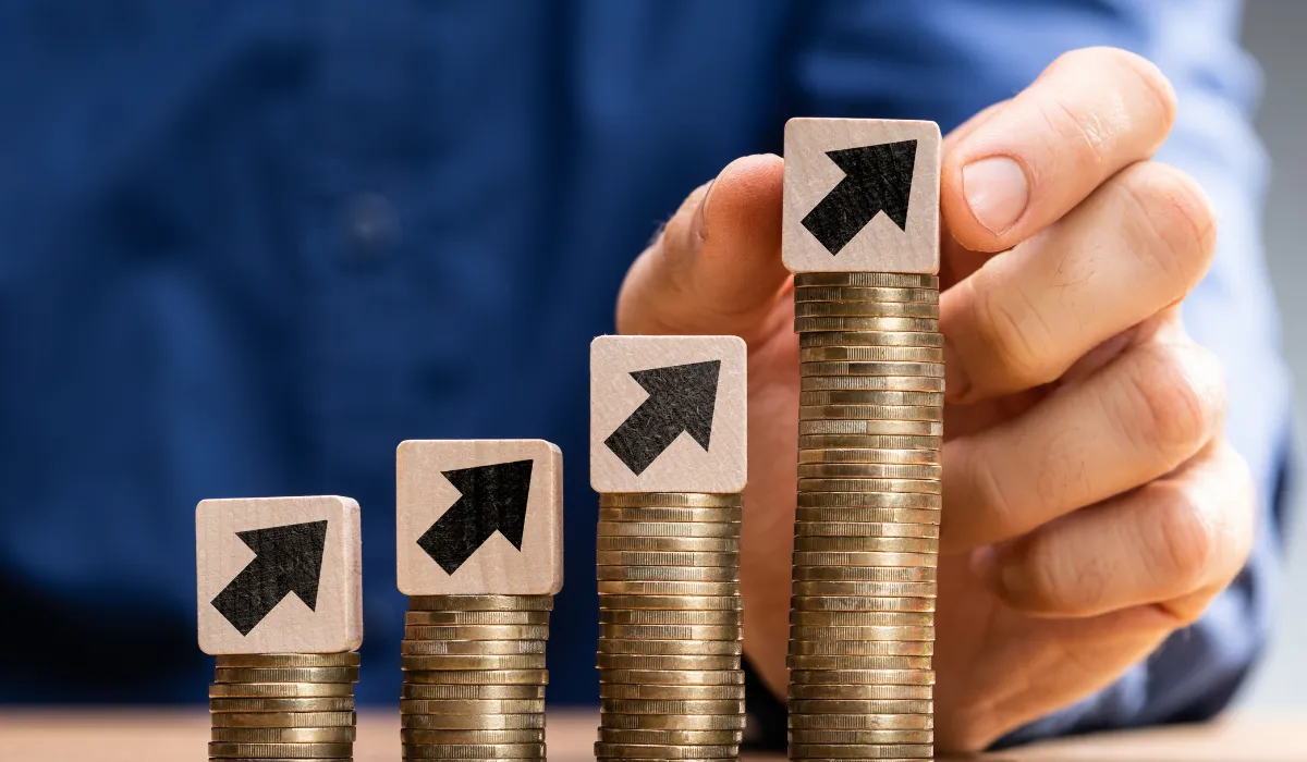 Stacked coins with upward arrows symbolizing financial growth and increasing costs.