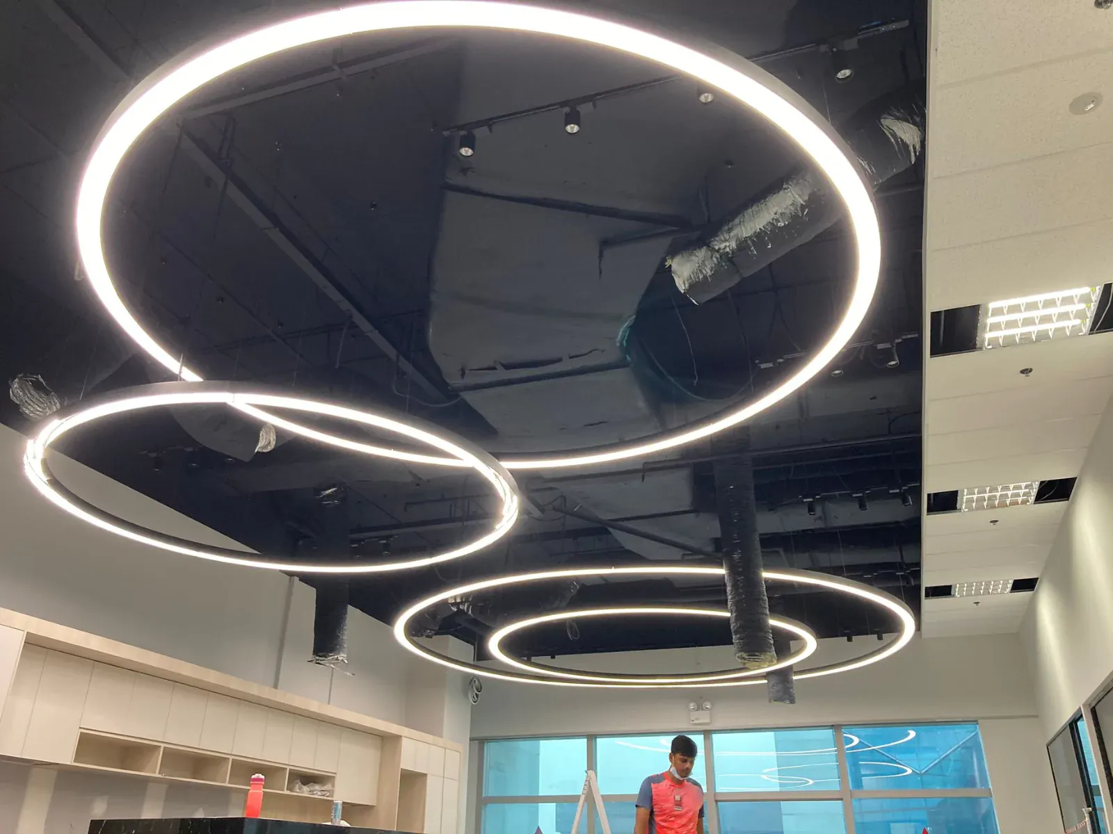 {"default":"Modern commercial space illuminated by large custom circular LED light fixtures, suspended from the ceiling in an overlapping design. These sleek, illuminated rings cast a bright glow, adding a futuristic and stylish touch to the interior."}