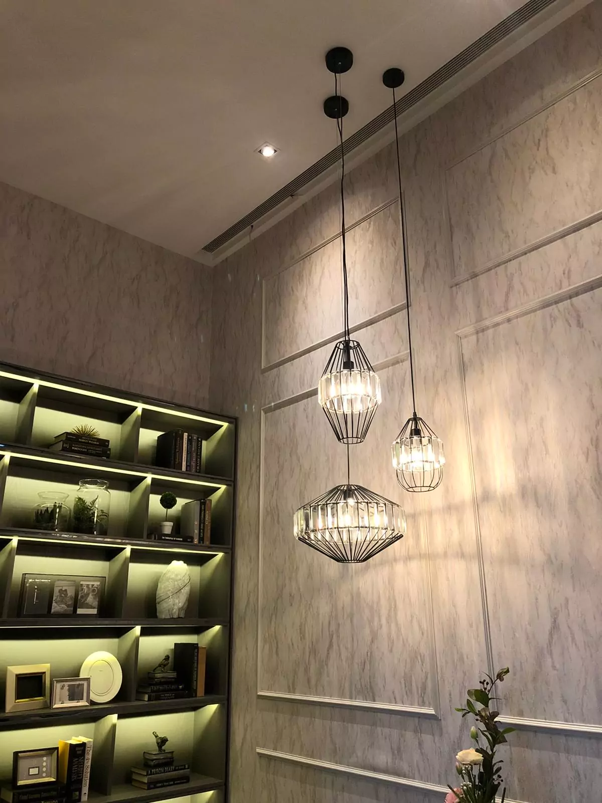 {"default":"Elegant interior corner with three pendant lights featuring intricate metal wire designs hanging from a dark ceiling, casting soft light on a taupe textured wall. "}