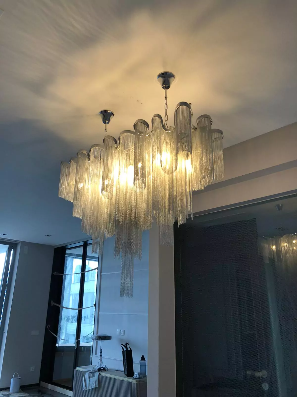 {"default":"Opulent chandelier featuring an array of cascading crystal strands that create a dramatic tiered effect, glowing warmly with light from multiple bulbs. "}
