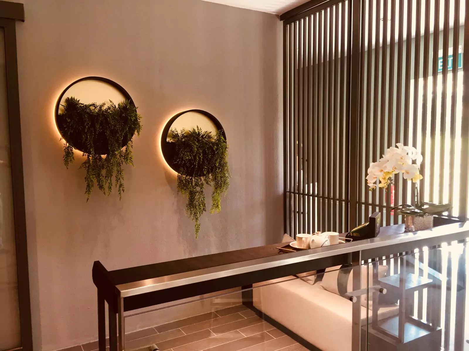 {"default":"Chic interior design featuring two circular gold lights with cascading green plants set against a muted gray wall, complemented by a sleek, dark wood console table and a cream bench."}