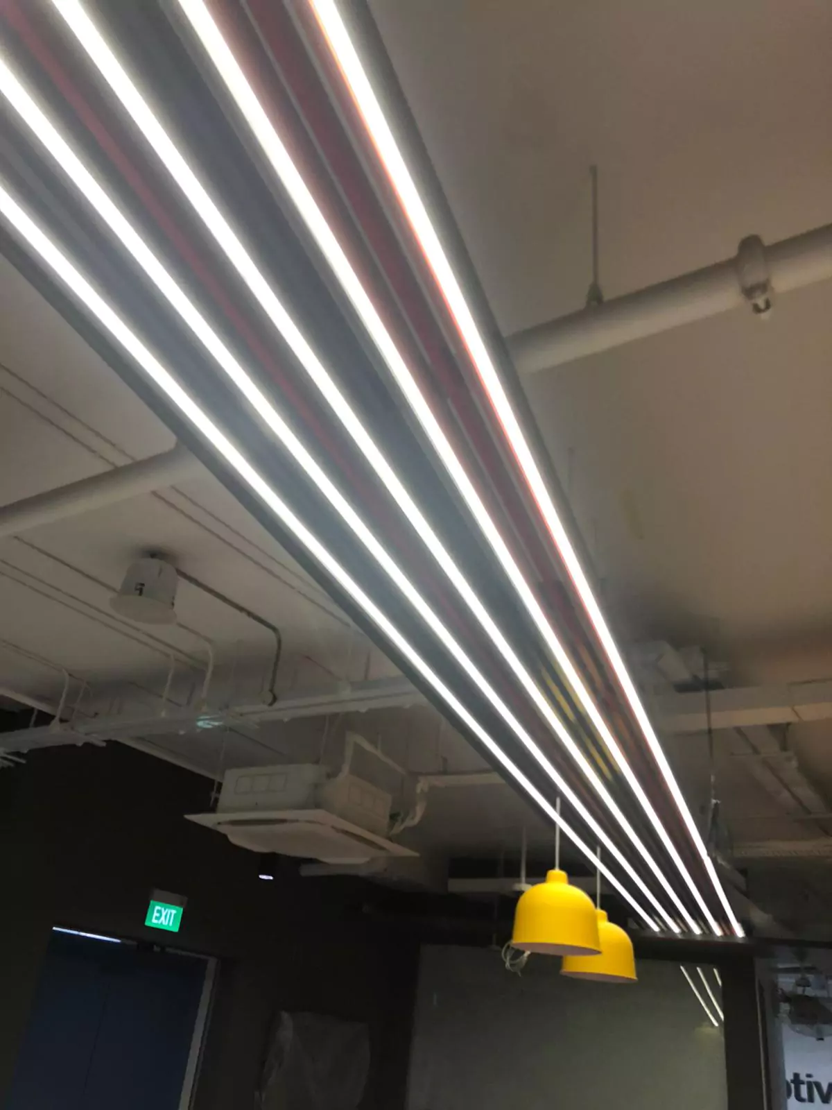 {"default":"Sleek office space illuminated by long, parallel LED light strips suspended from the ceiling, creating a modern and bright work environment. "}