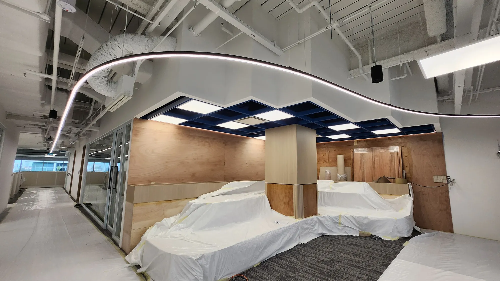 Curved LED strip lighting over a workspace with suspended ceiling and wood accents.