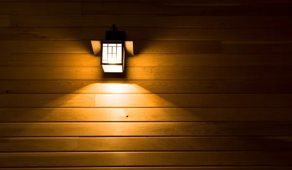 Warm wall-mounted outdoor light fixture glowing on wood siding