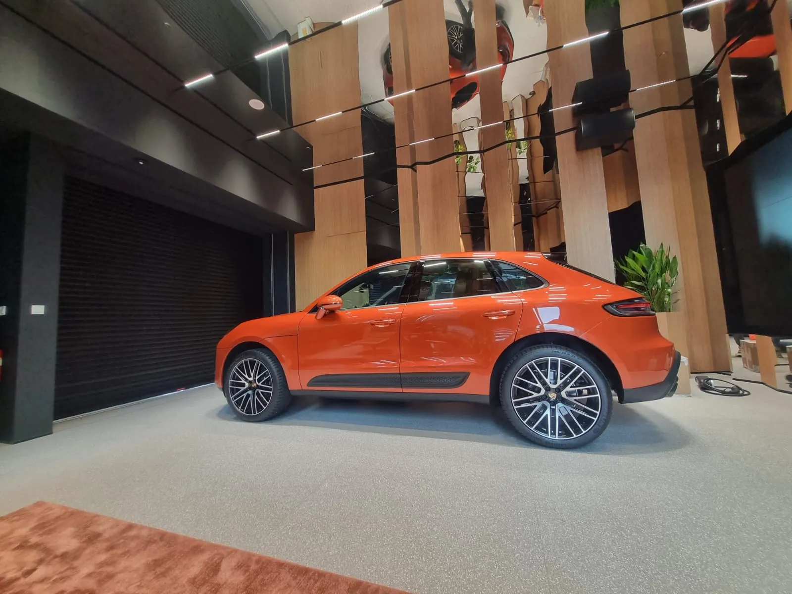 Orange Porsche displayed in a showroom with recessed tracklights and reflective ceiling design.