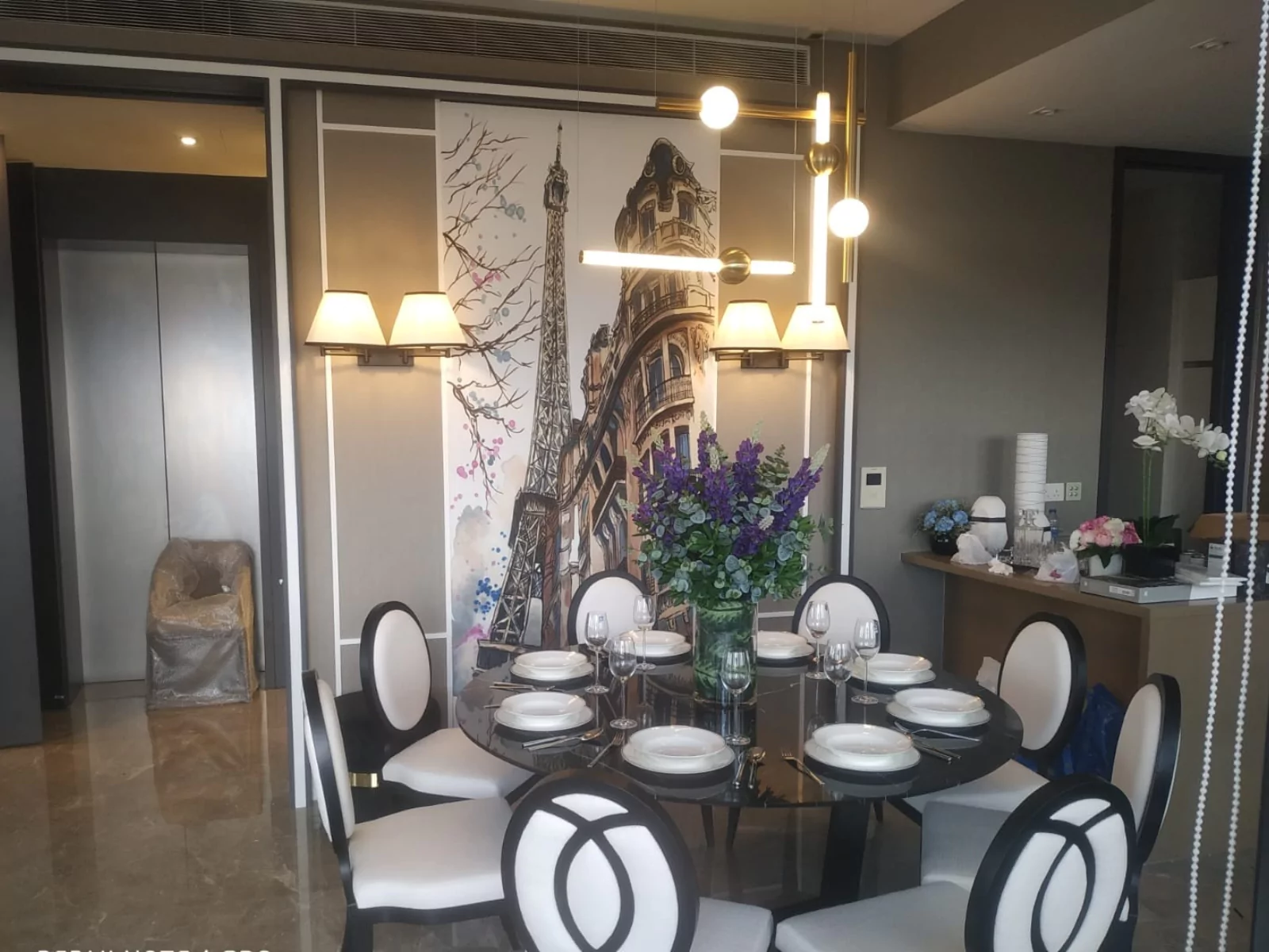 {"default":"Retro-inspired dining area featuring a circular table set for six, with elegant black and white chairs. Above the table hangs a classic chandelier with multiple lights, providing a warm ambiance."}