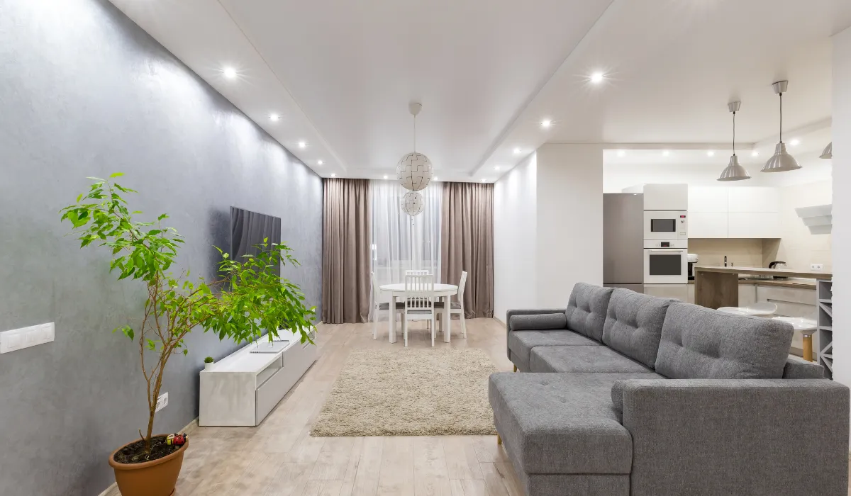 Modern studio apartment with warm ambient lighting, compact kitchenette, and vertical curtains enhancing the ceiling height.