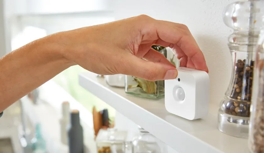 Hand placing a white motion sensor on a kitchen shelf