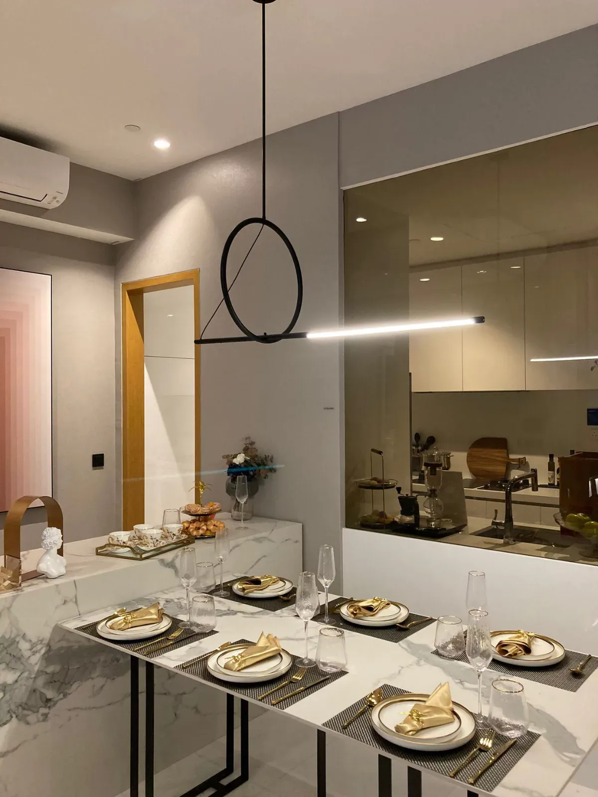 {"default":"Elegantly set dining table in a modern kitchen, featuring white plates and gold cutlery on a marble tabletop, complemented by a single circular pendant light. "}