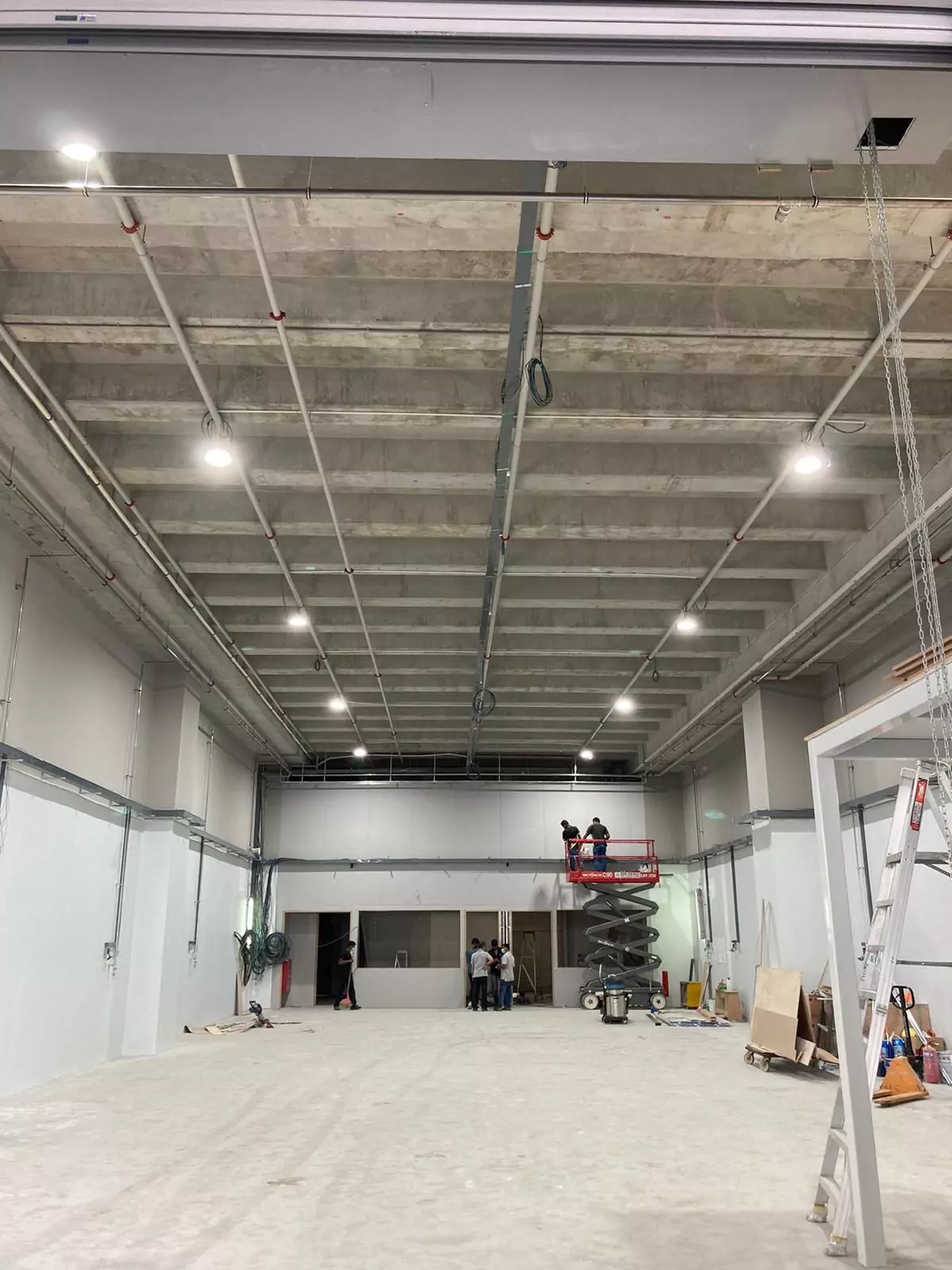 {"default":"Large warehouse space during the installation process, illuminated by bright floodlights mounted on the ceiling."}